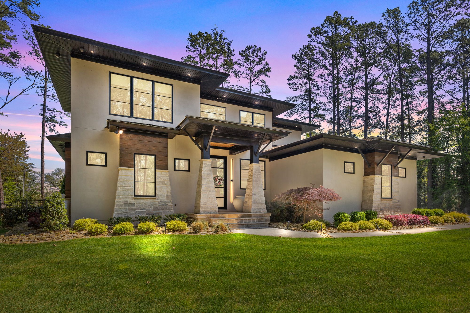 The front of the house at dusk, with stucco, stone columns and deep overhanging eaves under tall pines